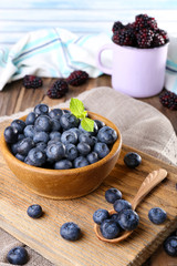 Wooden bowl of blueberries and metal mug of blackberries