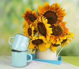 Beautiful sunflowers in pitcher with mugs