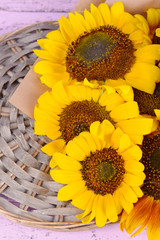Beautiful sunflowers on wicker stand on table close up
