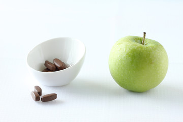 green apple and vitamin pills on white background