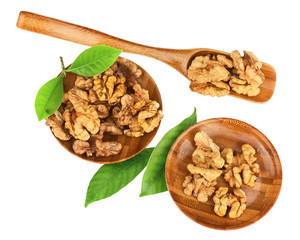 Handful of walnuts in wooden bowls, scoop and green leaves.
