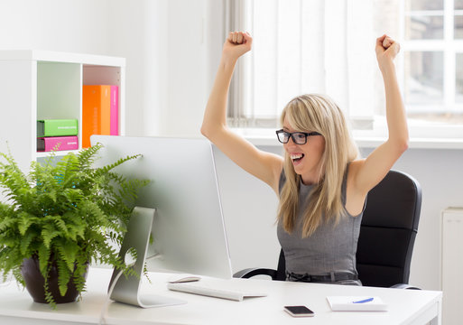 Happy woman sitting at her desk with arms up