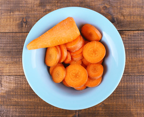 Slices of carrot in blue round bowl on wooden background