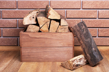 Wooden box of firewood on floor on brick background