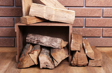Wooden box of firewood on floor on brick background