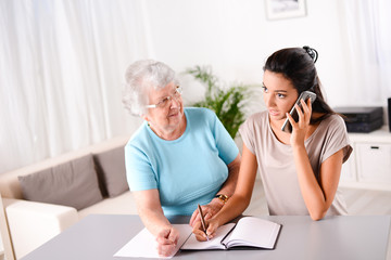 young woman helping old person for paperwork and telephone call
