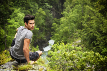 Naklejka na ściany i meble Handsome young man sitting in lush green mountain scenery