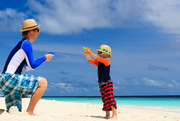 father and son playing with water guns on the beach