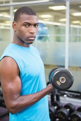 Fototapeta na wymiar Portrait of young man exercising with dumbbell in gym