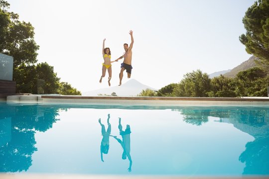 Cheerful couple jumping into swimming pool