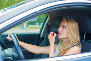 Fototapeta na wymiar Beautiful young woman applying make-up while driving car.