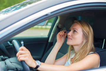 Fototapeta na wymiar Beautiful young woman applying make-up while driving car.