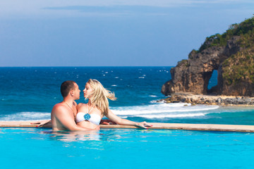 Fototapeta na wymiar young loving happy couple in the pool. Tropical sea in the back