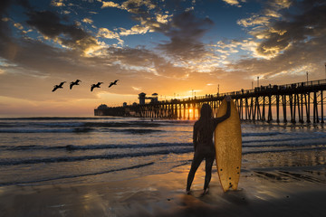 Een vrouwelijke surfer bewondert een zonsondergang in de buurt van de Oceanside Pier.
