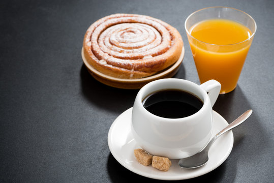 black coffee, sweet bun and orange juice on a black background