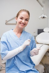 Dentist in blue scrubs smiling at camera holding tools