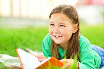 Fototapeta premium Little girl is reading a book outdoors