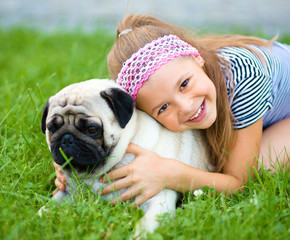 Little girl and her pug dog on green grass