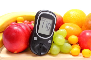 Glucose meter and fresh fruits on wooden cutting board