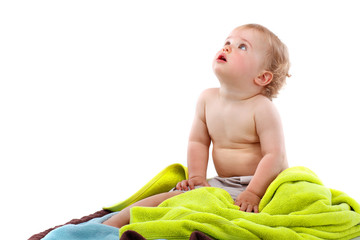 Small smiling blond curly boy sitting on colorful towels