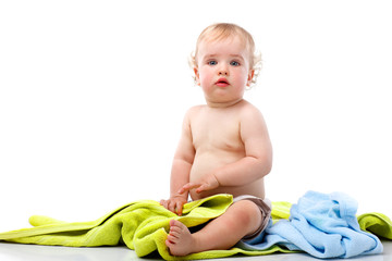 Small smiling blond curly boy sitting on colorful towels