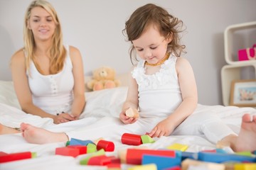 Obraz na płótnie Canvas Mother and daughter playing with building blocks on bed