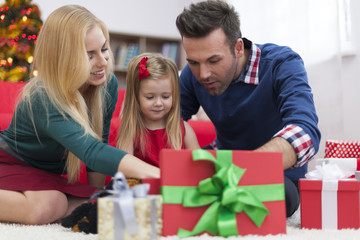Impatient little girl opening christmas presents with parents
