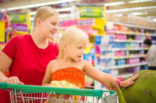 Young mother and adorable girl in shopping cart looks at giant j