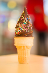 Ice cream cone with chocolate and rainbow color sprinkles on blu