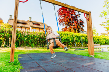 Cute toddler boy having fun on a swing on a nice summer day