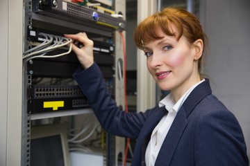 Pretty computer technician smiling at camera while fixing server
