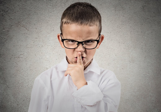 Boy giving be quiet gesture with finger on lips, grey background