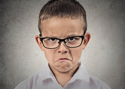 Unhappy sad, grumpy boy with glasses, grey wall background
