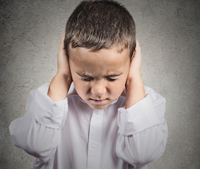 Boy Covers his Ears, hear no evil concept, grey background 