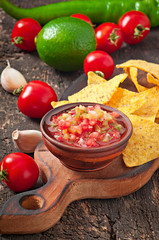 Mexican nacho chips and salsa dip in bowl on wooden background