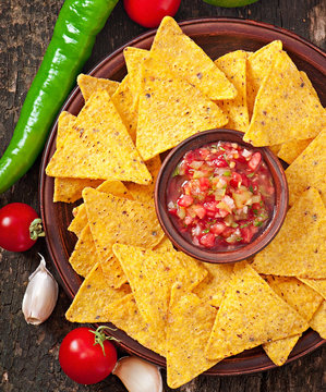 Mexican nacho chips and salsa dip in bowl on wooden background
