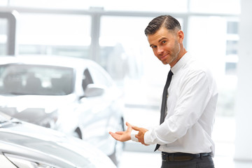 Naklejka na ściany i meble Salesman Standing at the Car Showroom and Showing New Cars