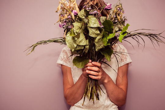 Young woman holding bouquet of dead flowers