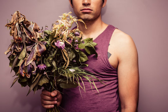 Young Man Holding Bouquet Of Dead Flowers