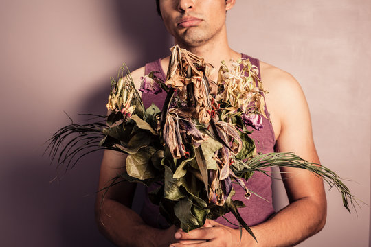 Young man holding bouquet of dead flowers
