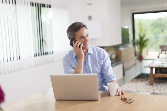 Attractive Man At Phone Using A Laptop At Home