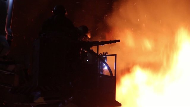 Silhouette of firemen at fire with hose and heavy flames showing