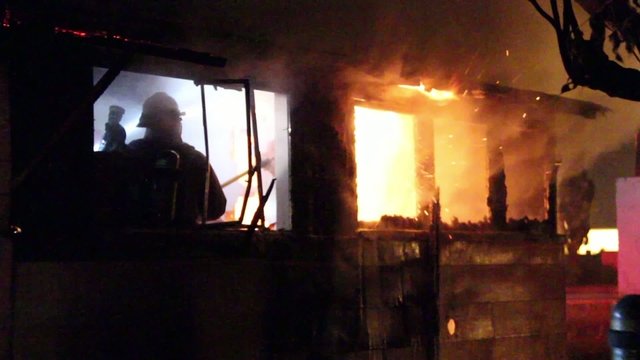 Fire fighters battling house fire at night with flames showing