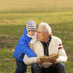 Grandfather and grandson reading a book outdoors