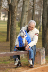 Fototapeta na wymiar Grandfather and grandson are looking tablet on bench outdoors