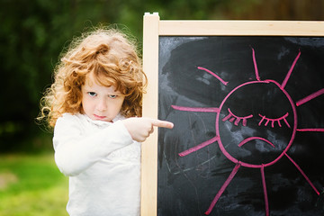 Little girl dissatisfied points on the board with a picture. Sad