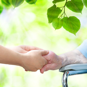 Senior woman in wheel chair holding hands with young caretaker