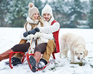 Paar mit Hund beim Rodeln im Winter