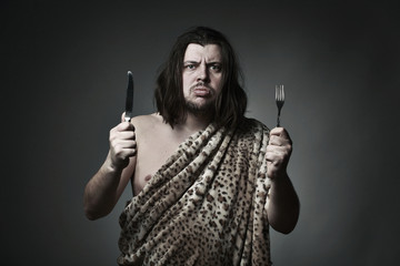 Hungry wild man wearing leopard skin hold fork and knife.