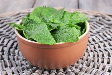 Brown round bowl of fresh mint leaves on a stand on wooden
